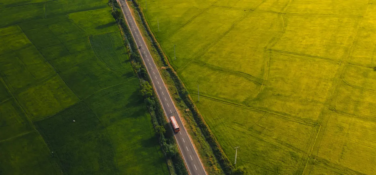 Bus driving through a road surrounded by green farmland landscape